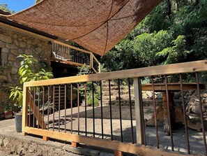 Un edificio de piedra con una escalera de madera, barandilla metálica y una zona sombreada con dosel tejido.