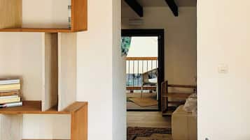 A room with a wooden staircase, a bookshelf, a potted plant, and a view of an outdoor balcony.