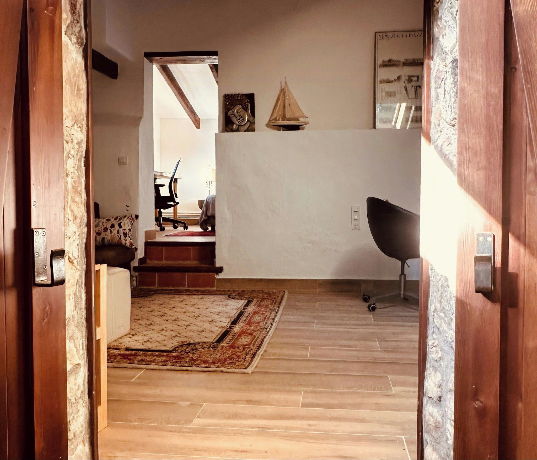 A room with a wooden floor, a patterned rug, a black chair, and a desk with a chair.