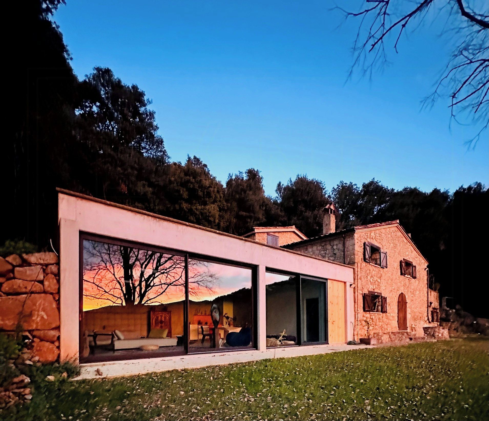 A modern house with a glass facade, stone walls, and a garden.