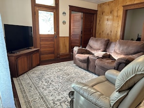 Ein Wohnzimmer mit Fernseher, zwei Sofas, einem gemusterten Teppich und Holztüren.