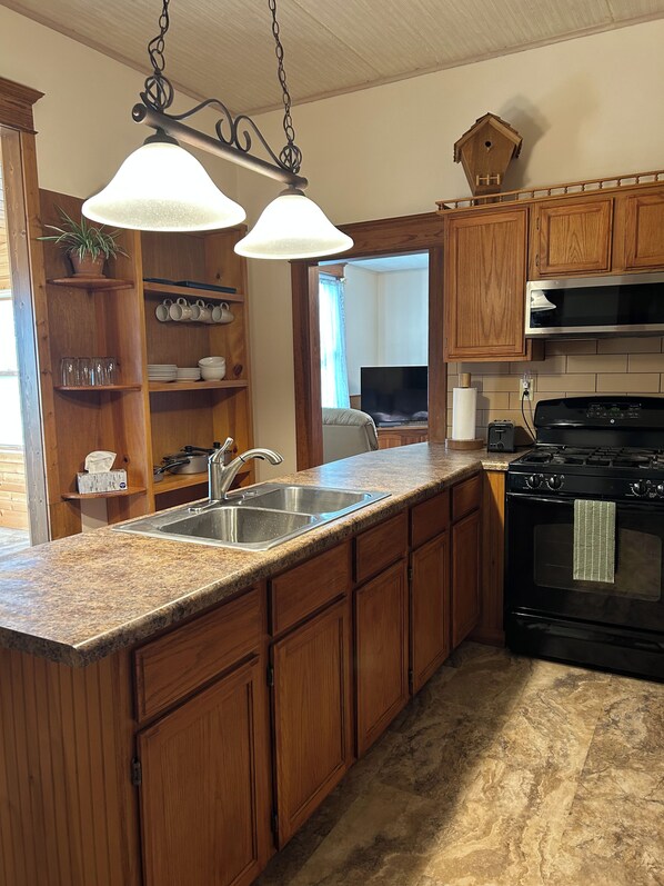 A kitchen with wooden cabinets, a granite countertop, a stainless steel sink, a black stove, and pendant lighting.