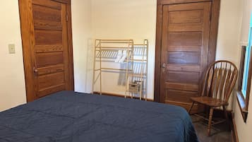 A bedroom with a bed, wooden wardrobe, a metal drying rack, and a wooden chair.