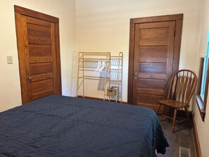 A bedroom with a bed, wooden wardrobe, a metal drying rack, and a wooden chair.