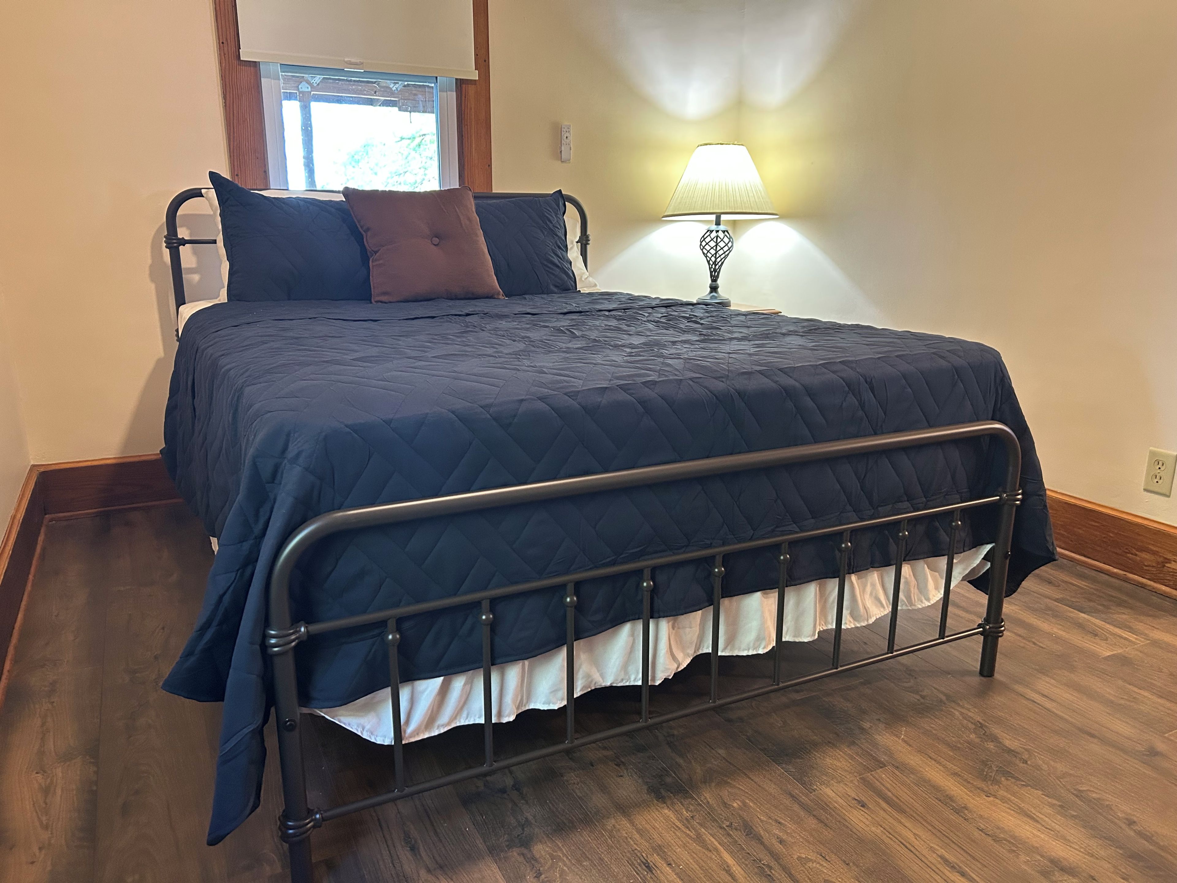A bed with a metal frame, a dark blue quilted bedspread, and a white skirted bed skirt.