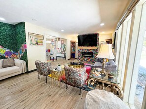 A living room with a fireplace, a television, and a dining area with colorful decor. - Chroma House: 3,000 sq. ft. 4BR Funky Art House w/Game Room-Sleeps 9 (Rogers)