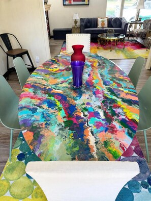 A dining table with a colorful abstract tablecloth, surrounded by green chairs. - Chroma House: 3,000 sq. ft. 4BR Funky Art House w/Game Room-Sleeps 9 (Rogers)
