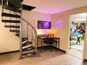 A room with a spiral staircase, a desk with a chair, a wall-mounted TV, and a colorful wall. - Chroma House: 3,000 sq. ft. 4BR Funky Art House w/Game Room-Sleeps 9 (Rogers)