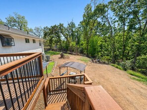A wooden deck with a metal railing, a covered outdoor seating area, and a dirt path leading to a house with a white exterior. - Chroma House: 3,000 sq. ft. 4BR Funky Art House w/Game Room-Sleeps 9 (Rogers)