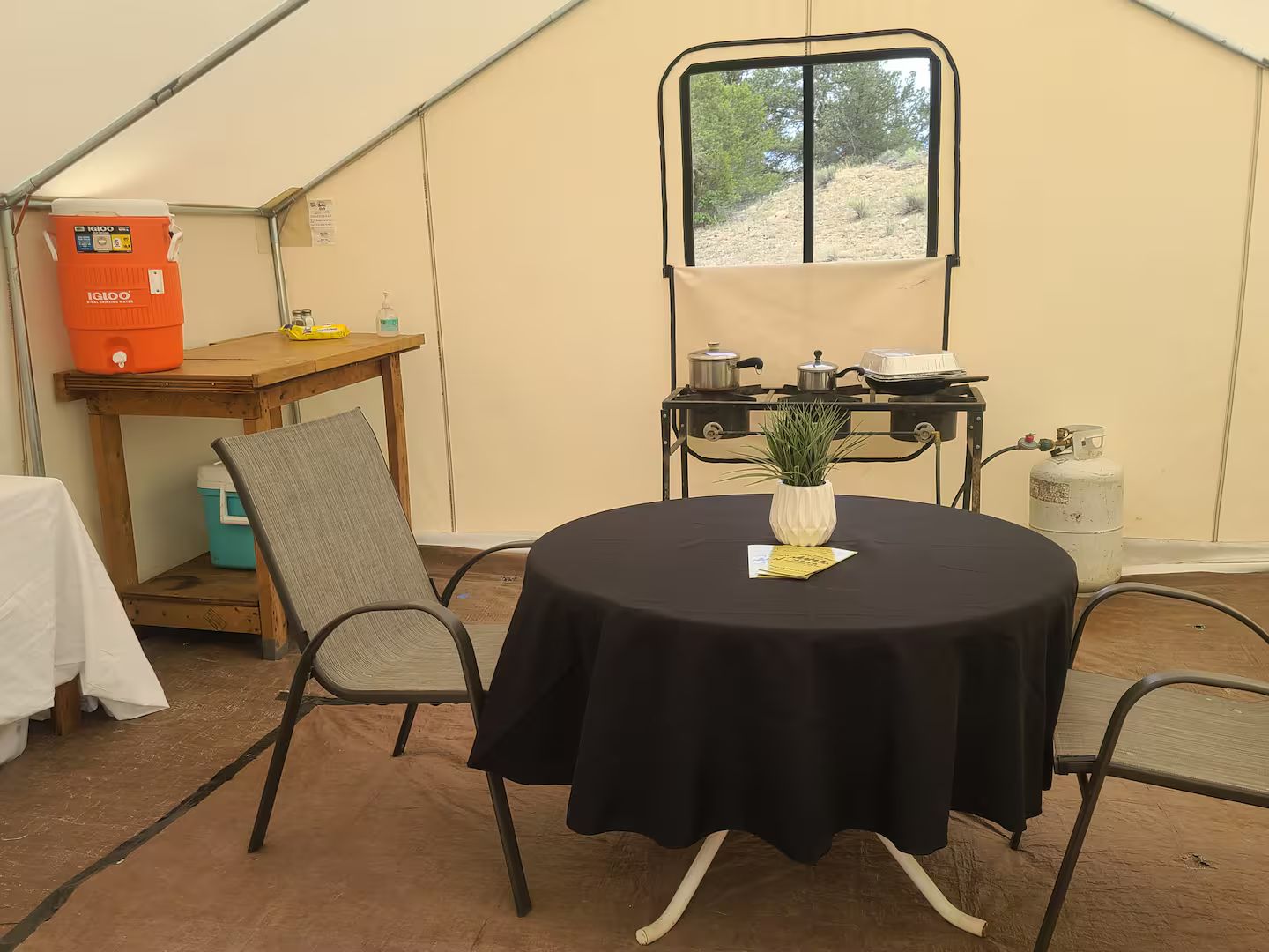 Een tent met een ronde tafel, stoelen, een raam en een tafel met een plant.