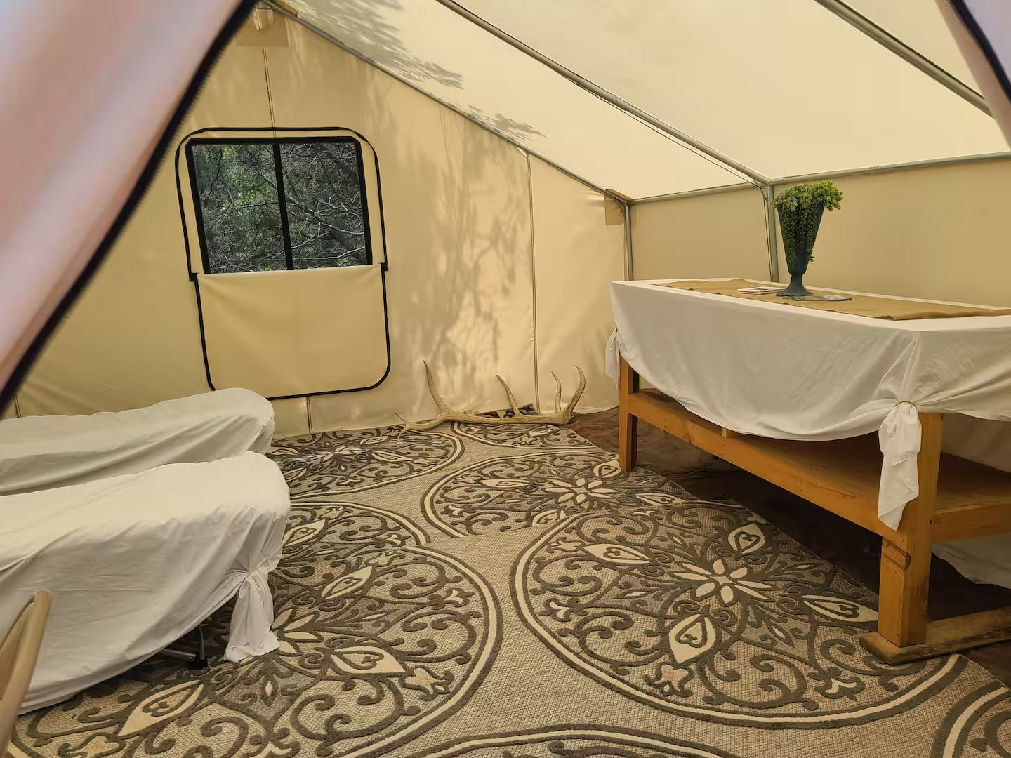 Een tent met een bed en een tafel, een raam en een vloer met een patroon.