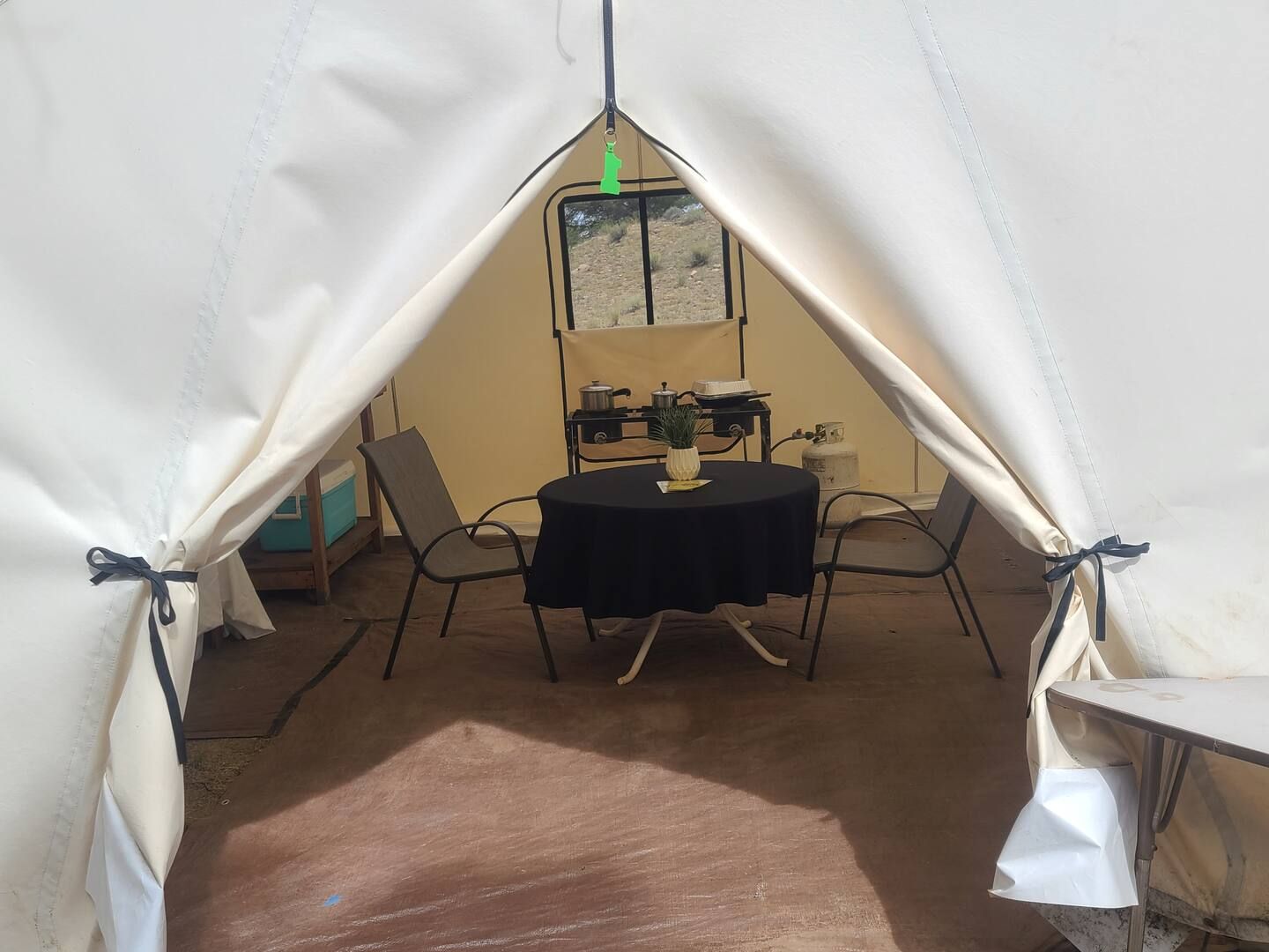 A tent with a table and chairs inside, a window, and a green hanging object.