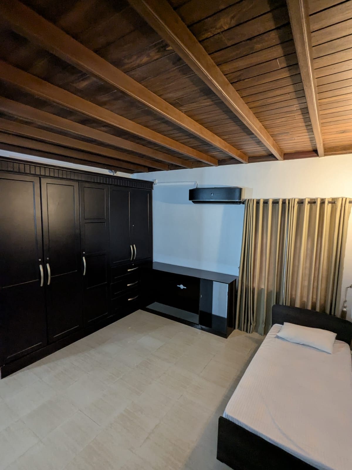 A bedroom with a bed, dark cabinets, a flat-screen TV, and a ceiling fan.