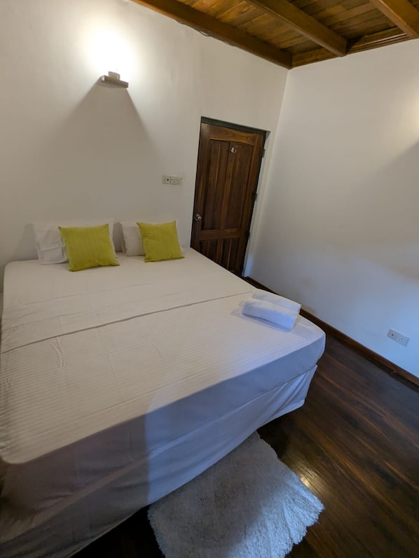 A bedroom with a bed, pillows, a wooden door, and a light fixture on the wall.