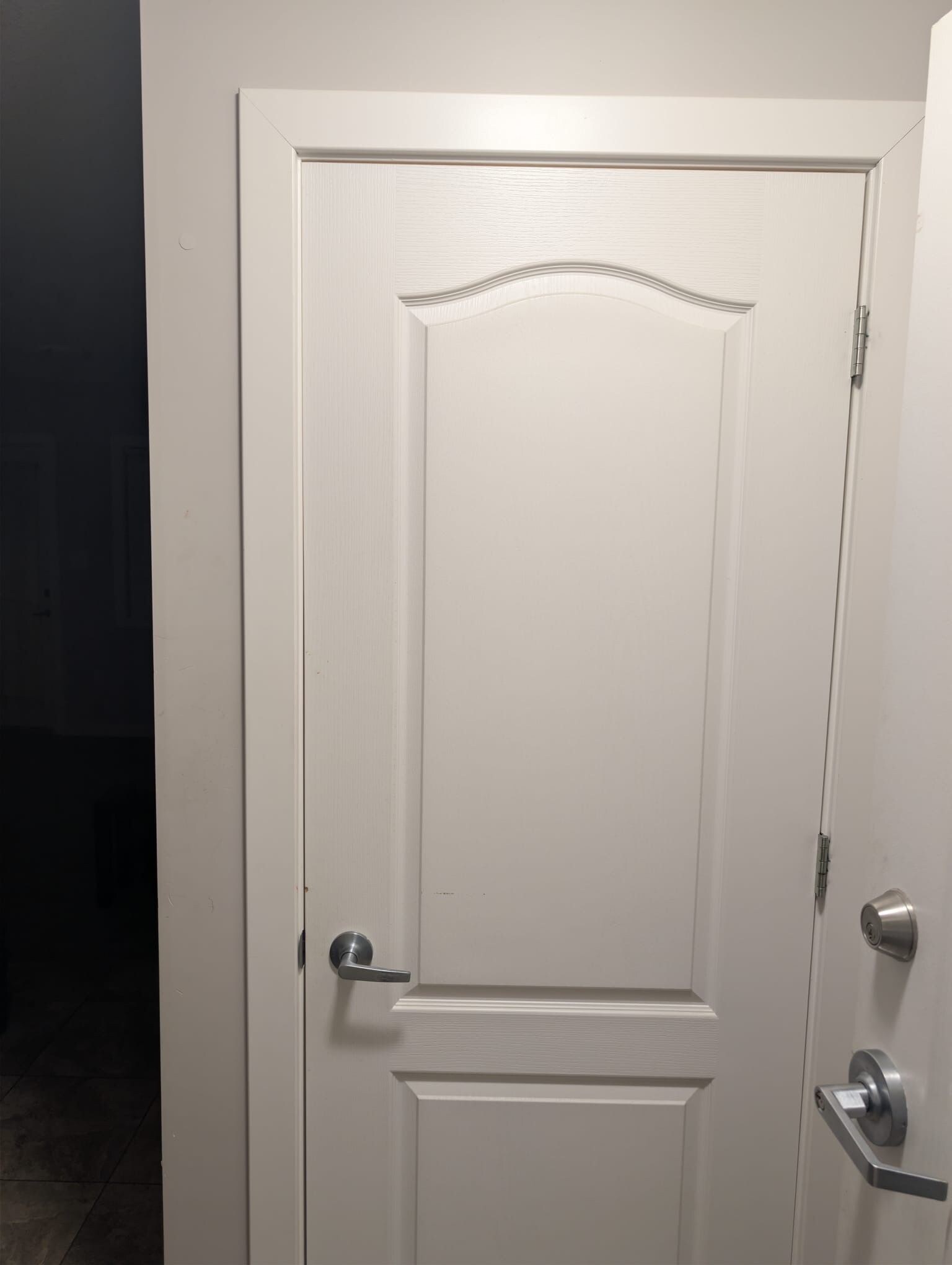 Una puerta blanca con manija plateada y cerradura con llave.