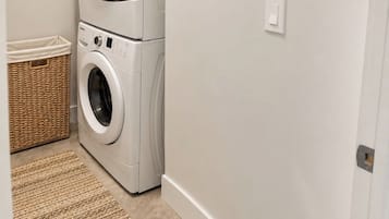 A laundry room with stacked front-loading washers and dryers, a wicker basket, and a beige rug.