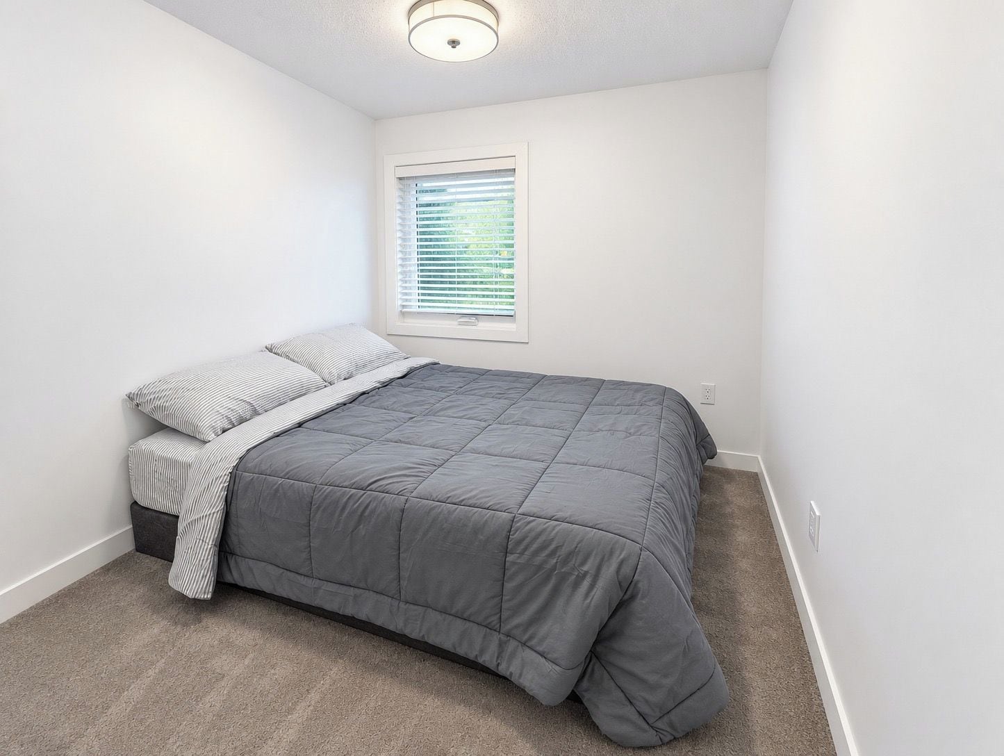 A bedroom with a bed, a window with blinds, and a ceiling light.