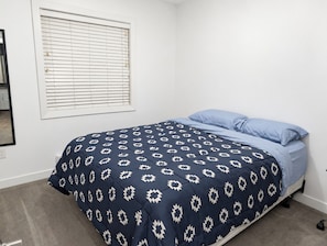 A bedroom with a bed, a window with blinds, and a carpeted floor. - Spacious Yorkton Apartment (Yorkton)