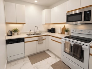 A modern kitchen with white cabinets, stainless steel appliances, and a marble floor. - Spacious Yorkton Apartment (Yorkton)
