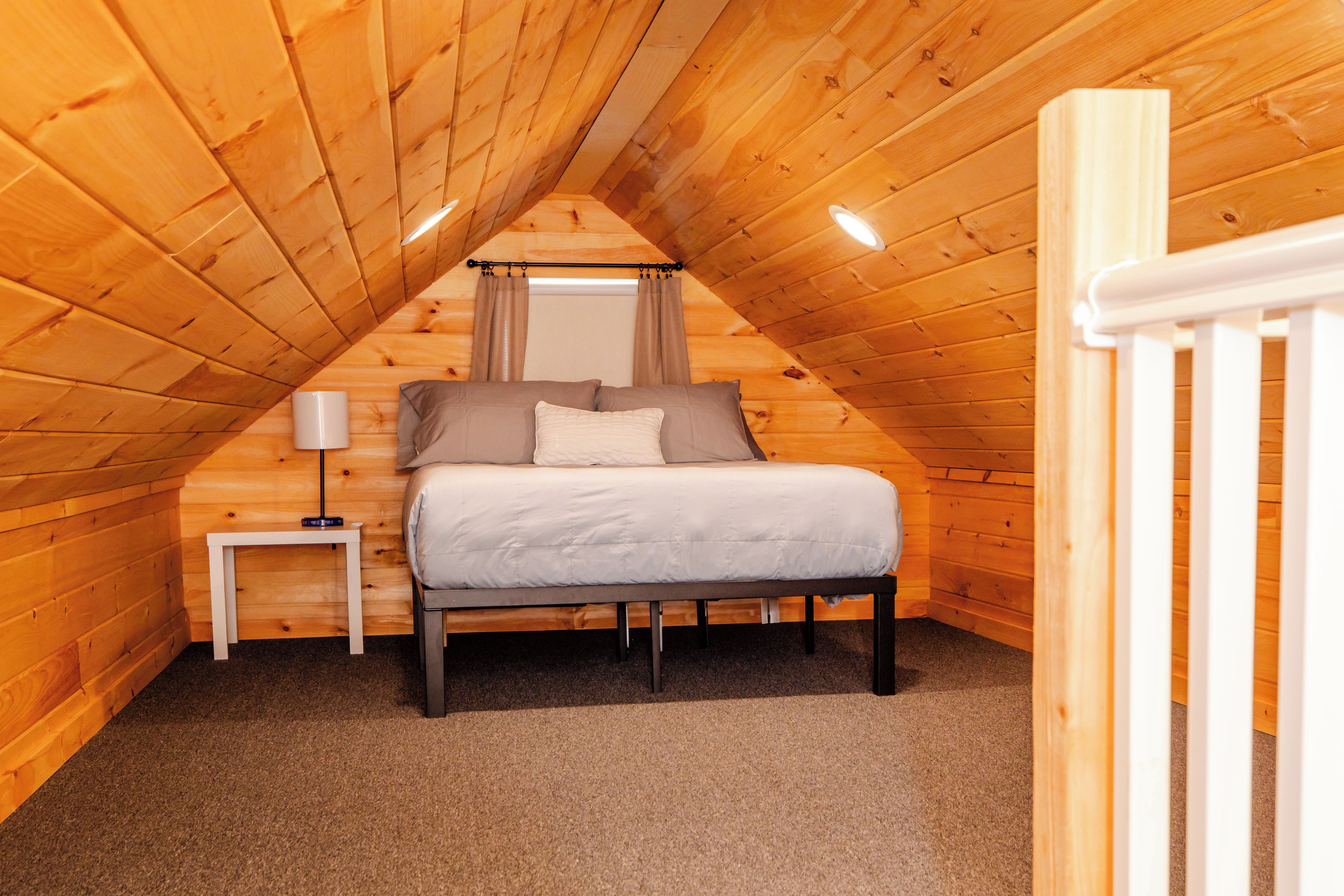 A bedroom with a sloped ceiling, a bed, a bedside table, and a lamp.