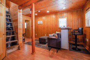 Interior acollidor d'una cabana amb terra de fusta, un sofà, un escriptori amb cadira i una escala.