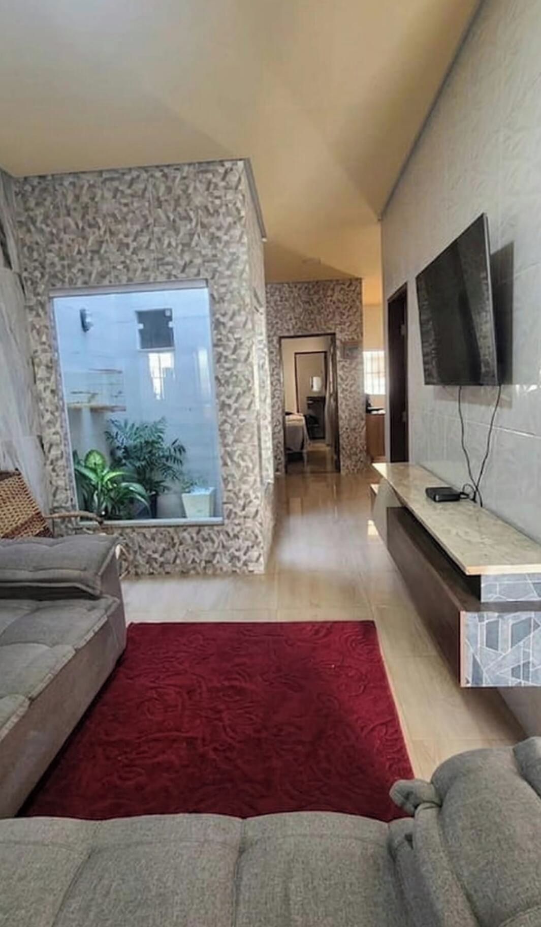 Ein modernes Wohnzimmer mit großem Fenster, Flachbildfernseher und einem roten Teppich.