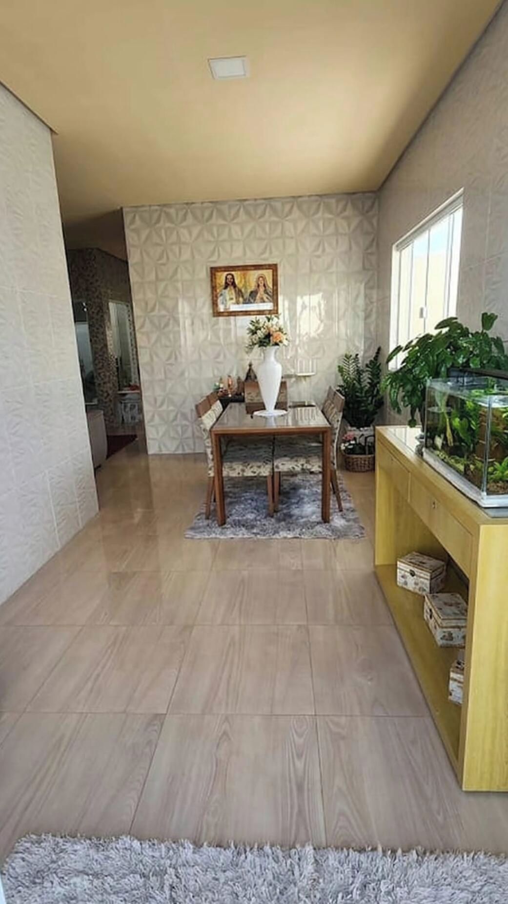 Un coin repas comprenant une table, des chaises, un vase avec des fleurs, un tableau encadré au mur et une plante en pot.