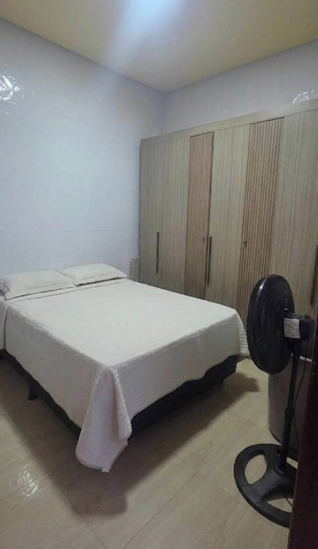 Une chambre à coucher avec un lit, une armoire et un ventilateur sur pied.