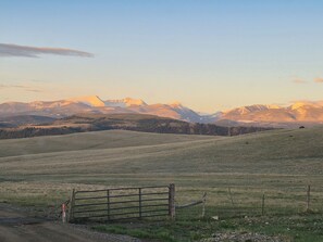 A rural landscape with a metal gate, a dirt path, and a mountain range in the background.
