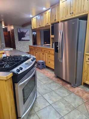 A modern kitchen with wooden cabinets, stainless steel appliances, and a tiled floor. - Rustic Farmhouse (Burns)