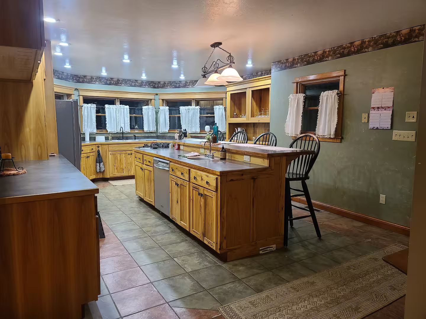 A kitchen with wooden cabinetry, a central island, and a dining area with chairs.