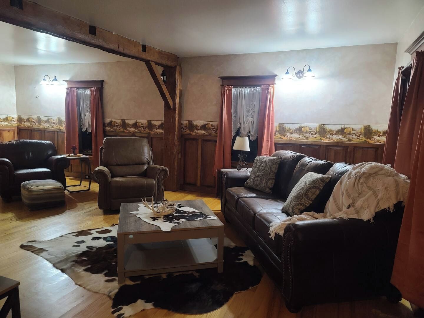 A living room with a leather sofa, a leather armchair, a coffee table, and a cowhide rug.