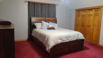 Une chambre à coucher avec un lit en bois, une moquette rouge, une armoire en bois et un ventilateur de plafond.