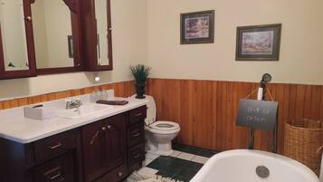 Une salle de bain avec un lavabo blanc, un meuble-lavabo en bois foncé, des toilettes blanches et une baignoire. Deux tableaux encadrés sont accrochés au mur, et une pancarte indique : « Hors service ».