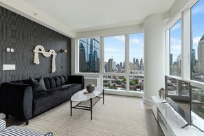 Ein modernes Wohnzimmer mit einer schwarzen Couch, einem weißen Couchtisch und einem großen Fenster mit Blick auf die Stadt.