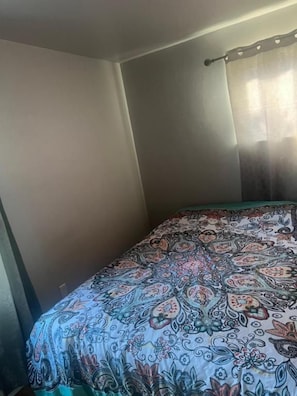 A bedroom with a bed, a window with curtains, and a wall.