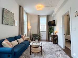 Ein modernes Wohnzimmer mit einem blauen Sofa, einem Glastisch und einem Flachbildfernseher.