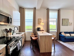 A compact kitchen with a central island, bar stools, a coffee machine, and a view of the outdoors. - DWTN New Haven | King Bed | Free Parking | Gym (New Haven)