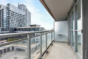 A balcony with a view of high-rise buildings, a glass railing, and a concrete floor. - Luxe Downtown Suite Steps to Entertainment District (Toronto)