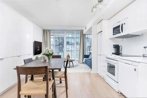 A modern kitchen with white cabinets, a dining table with chairs, and a large window. - Luxe Downtown Suite Steps to Entertainment District (Toronto)
