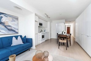 A modern apartment with a blue sofa, a dining area, and a kitchen. - Luxe Downtown Suite Steps to Entertainment District (Toronto)