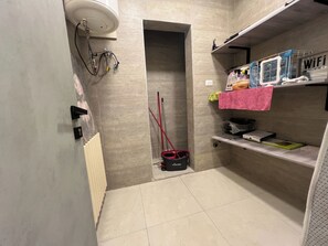 A bathroom with a shower, a toilet, a radiator, and a shelf with toiletries. - Cozy 2-Bedroom Apartment with 3 Beds & 2 Bathrooms (Amman)