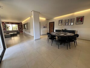A modern living room with a sofa, a dining table set for six, and a kitchen area with a window. - Cozy 2-Bedroom Apartment with 3 Beds & 2 Bathrooms (Amman)