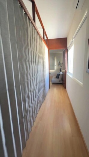 A hallway with a wooden floor, a grey textured wall, and a glimpse of a room with a bed and a window. - Private Pool House in Oaxaca (Oaxaca de Juárez)