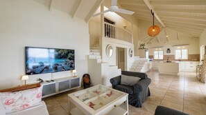 A spacious living area with a large flat-screen TV, a sofa, a coffee table with decorative items, and a staircase leading to an upper level. - Villa Azure Horizon - Oceanfront & Private Pool - Coral Estate Resort - Privacy (Coral Estate)