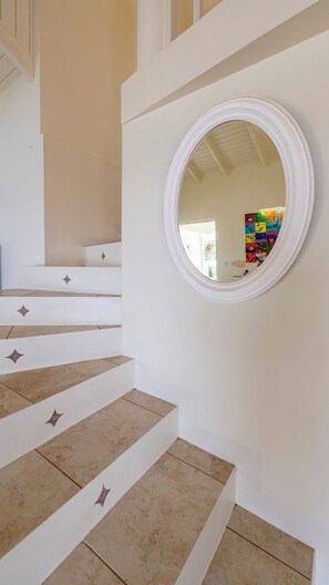 A staircase with beige steps and white walls, leading to a room with a round mirror and a colorful wall art piece. - Villa Azure Horizon - Oceanfront & Private Pool - Coral Estate Resort - Privacy (Coral Estate)