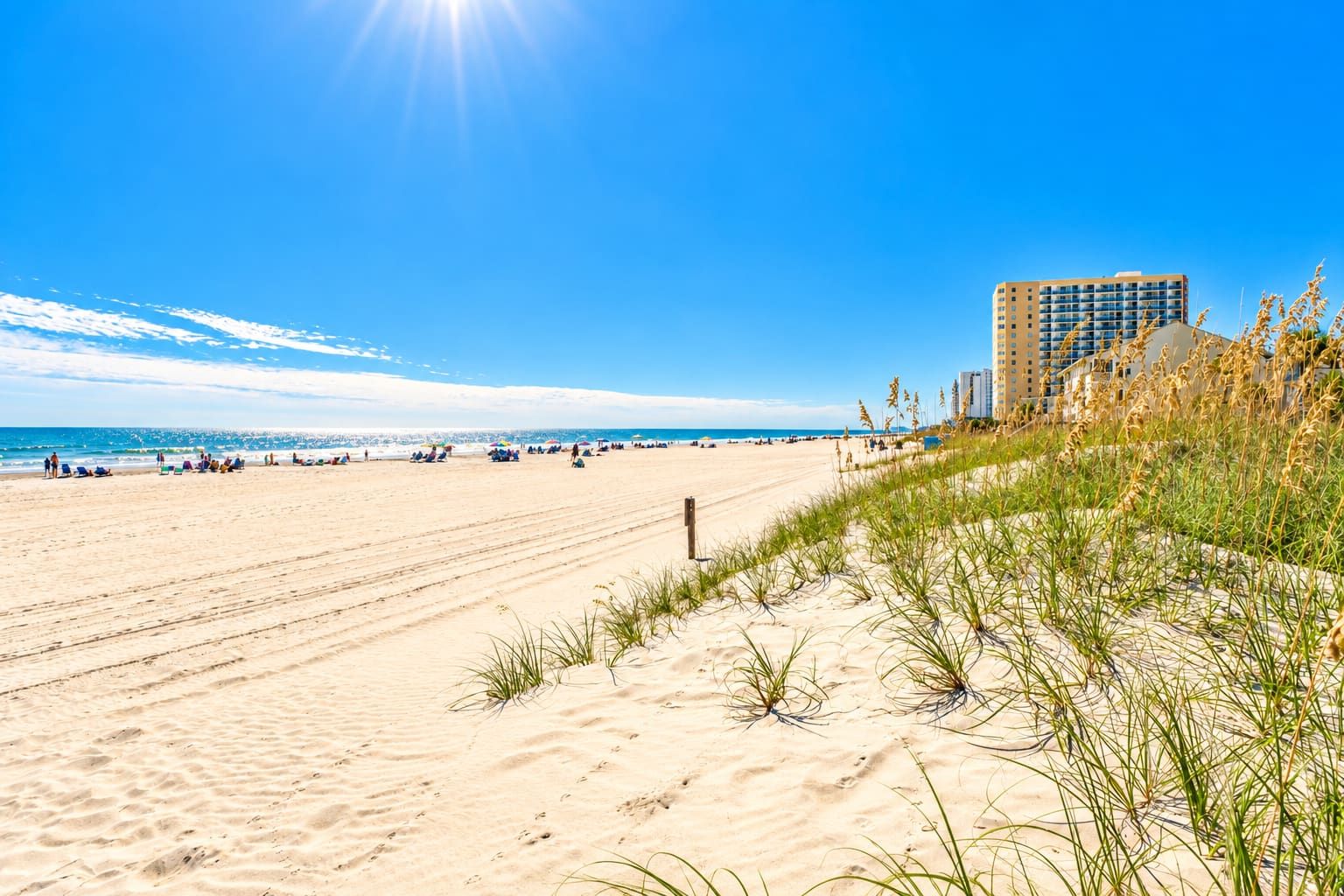 A beach with a clear sky, sandy shore, and a building in the background.