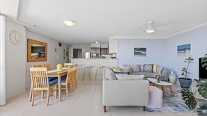 Una sala de estar moderna con un sofá gris, una mesa de comedor de madera y una cocina al fondo.