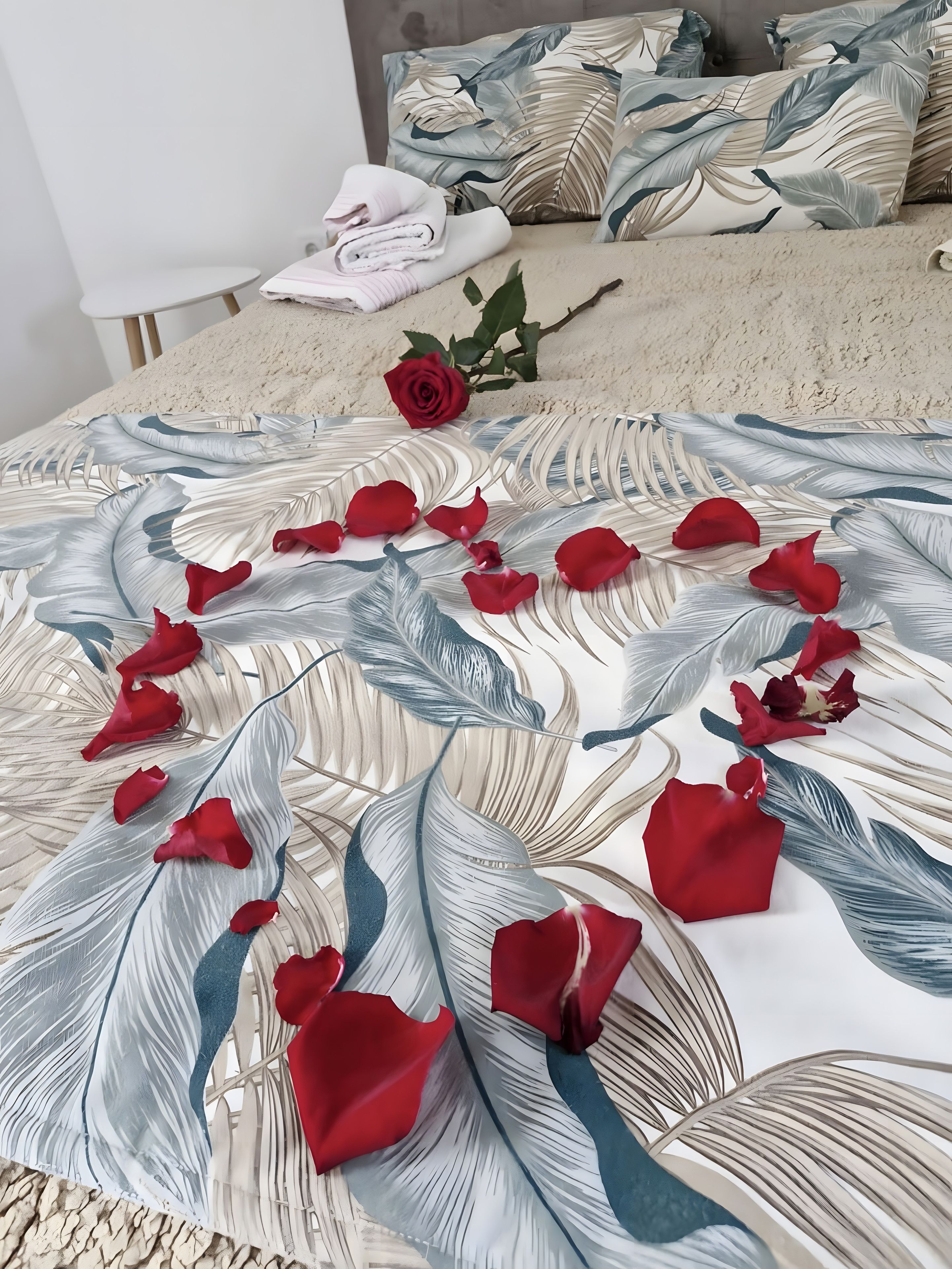A bed with a floral-patterned bedspread, a red rose, and folded towels.