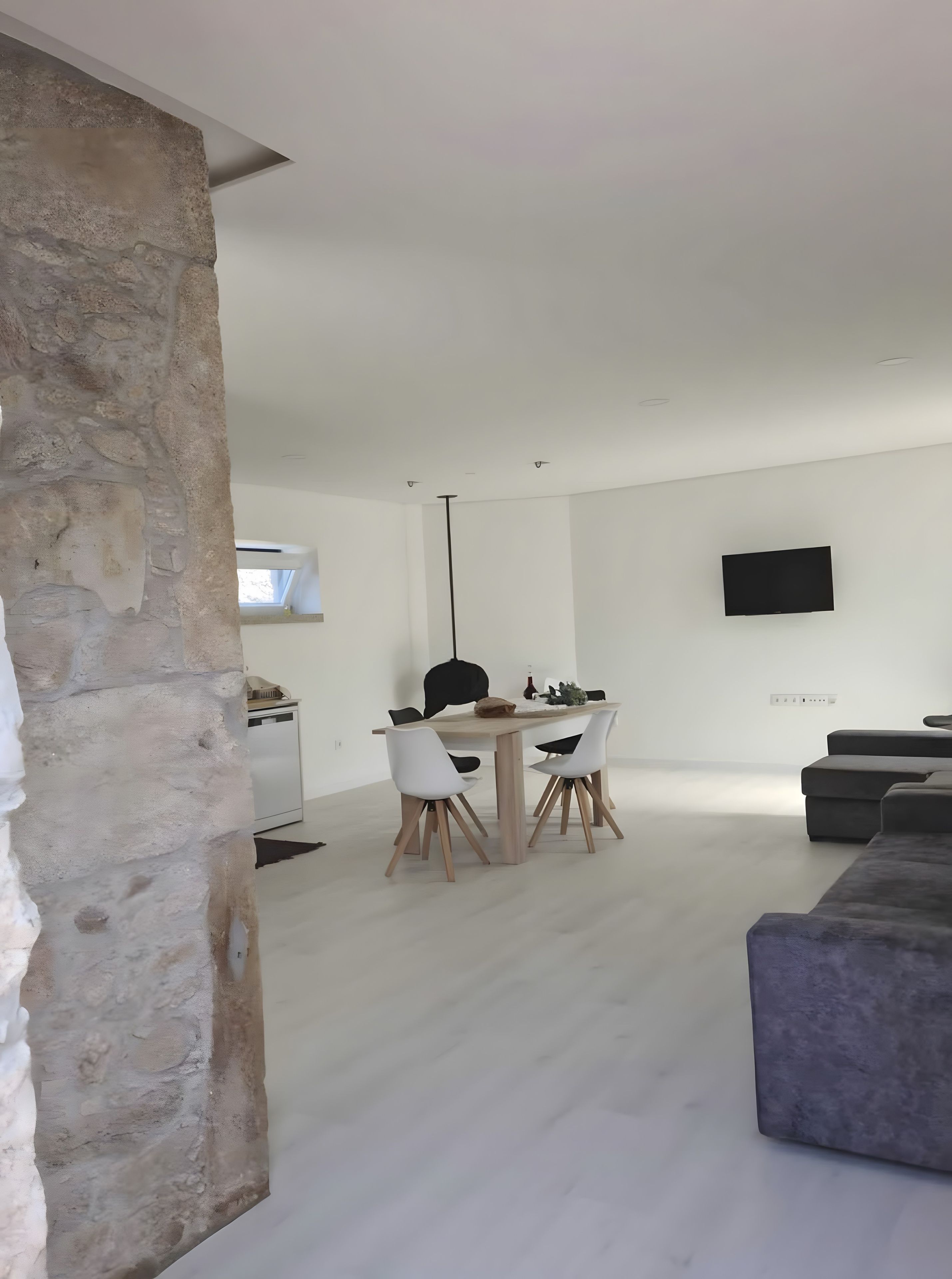 A modern living space with a stone accent wall, a dining area with a table and chairs, a flat-screen TV mounted on the wall, and a grey sectional sofa.